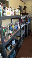 Photo showing metal shelving units with various bottles, spray containers, and cleaning supplies on multiple shelves.
