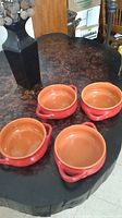 Four reddish terracotta glossy bowls with a natural brown interior on a dark wood table.