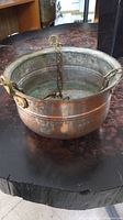 Side view of the copper cauldron showing patina and attached brass chains for hanging.