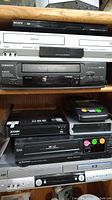Shelf full of stacked electronics including Sony DVD player, Orion VCR, Zosi digital recorder, and other players.