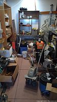 Full view of garage corner showing shelving units with various tools, equipment, and storage containers including an electronic rototiller in the center.