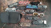 Overview of most glasses and cases on a brown patterned surface including reading glasses, sunglasses, and various carrying cases