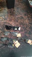 Full view of four pairs of reading glasses and one pair of polarized sunglasses laid flat, showing tags on each pair.