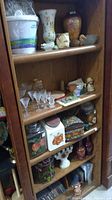 Wooden shelf containing various collectible and antique glassware items including vases, figurines, glassware, cookie jars, and other small collectibles