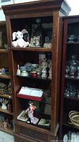 Full view of wooden shelf filled with assorted collectibles including stuffed rabbit toy, porcelain figurines, ceramic cups, decorative boxes, and glassware.