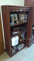 Full wooden bookshelf with items arranged on four shelves including bread maker and decorative items.