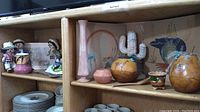 Two wood shelves containing Southwestern Native American inspired art and craft items including dolls, pottery, gourds, and vase.