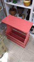 Photo of pink wooden shoe rack with shelf and slatted sides, empty and standing on tile floor.