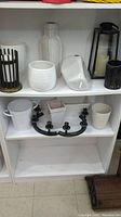 White and black decor pieces displayed on shelves showing vases, candle holders, and containers.