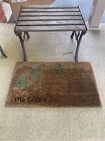 Full view of the wood and cast iron side table with outdoor mat below it. Both items are positioned on a concrete floor, showing condition and scale.