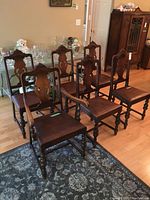 Six dining chairs with dark wood finish and leather-like upholstery placed on a patterned rug and hardwood floor, showing overall design and wear.