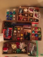 Top view of boxes with assorted Christmas tree decorations, including vintage and modern glass baubles, decorative bows, and packaged Christmas lights.