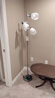 Full view of the steel post floor lamp with three white glass shades placed in a corner of a room, showing its height and overall design.
