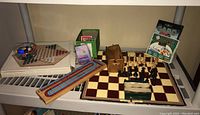 Overview showing chessboard with chess pieces, cribbage board, checkers pieces box, marbles and jacks in clear bowl, decks of cards, and PC card game box