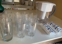 Photo showing 10 clear water glasses with two styles and Brita water filter jug with two filter packages