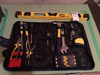 Full kit arranged on table showing Stanley Fat Max level and a black tool roll with multiple hand tools including screwdrivers, pliers, hammer, wrench, tape measure, scissors, and a set of small screwdrivers.