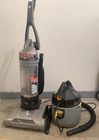 Hoover WindTunnel T-Series upright vacuum and Stinger Wet/Dry shop vacuum shown side by side on concrete floor.