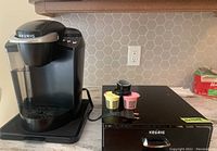 Keurig coffee maker next to pod storage drawer with three reusable pods on top