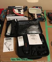 Lot overview showing the Conair hair dryer box, Remington hair clippers in case, Hopo50 massage gun case, hand mirror, and hanging organizer on table