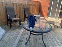 Glass-top rectangular table with closed navy umbrella resting on top and two chairs behind