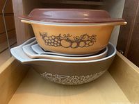 Photo showing 4 nested mixing bowls and one lidded casserole dish stacked inside a wooden drawer.