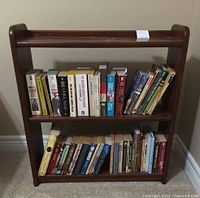 Front view of the dark stained pine bookshelf filled with paperback books on two shelves.
