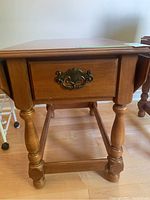 Front view of wood side table showing drop leaves, drawer, and turned legs.