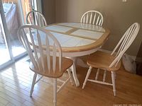 Dining table and four chairs set from a slight angle near sliding glass door, shows white tile inlay table top and natural wood edges and seats