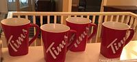 Four red Tim Hortons mugs with white 'Tims' logo displayed side by side showing overall design and condition.