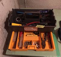 Photo showing plastic black tool tote with removable orange drawer containing pliers, nails, screws, tape and measuring tape.