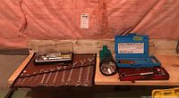 Overview of all tool items on surface: combination wrenches in fabric roll, flashlight, screwdriver bit set in blue case, red ratchet tool case.