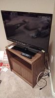 Samsung 32-inch TV on faux wood cabinet with remote visible on top shelf.