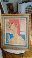 Frontal view of an unsigned painting on board of a woman with bright red hair in profile, including frame and setting context.