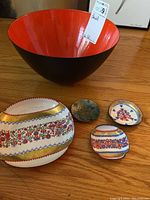 Photo showing large black and red metal bowl with 1 large decorative tray and 3 small trays on wooden surface