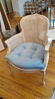 Front view of chair showing white painted wood frame, cane back and blue tufted cushion