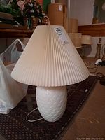 Front view of the white ceramic table lamp with pleated paper shade placed on a patterned carpet.