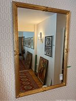 Mirror hanging on a wall reflecting hallway with framed pictures and stairs, showing full view of the mirror and frame design.