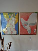 Photo showing both framed watercolor paintings hung side by side on a wall.