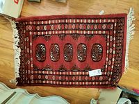 Full view of the red wool hand-knotted rug with symmetrical central oval medallions and fringe edges on a wooden floor.