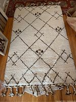 Full view of off-white wool rug with brown/black diamond lattice pattern laid on hardwood floor