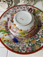 Close-up of the teacup upside down on a matching plate showing the colorful Japanese/Asian floral and figure scene and bottom marking