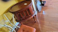 Side view of a round wooden bar cabinet showing the decorative beaded trim and curved legs next to other furniture items.