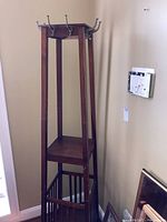 Full view of wooden coat rack including base umbrella stand and display shelf in corner of room.