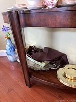 Gold tone chargers and smaller side plates stacked on lower shelf of wooden stand with maroon table runner partially visible.