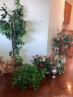 Full view of approximately eight faux plants with various foliage and vases arranged on floor against a wall.