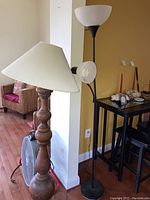 Image showing two floor lamps side by side with a wooden floor lamp in front and a black metal lamp behind it, a Patton fan partially visible behind the wooden lamp.