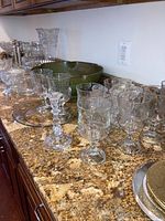 Wide view of multiple glassware items on countertop including glasses, green bowl, and candle holders.