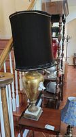 Large black and gold table lamp on a wooden surface near staircase, detailed view of lamp and shade