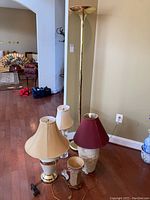 Set of five lamps including four table lamps and one floor lamp shown grouped together in a room near a wall outlet, showcasing variety in size and style.