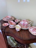 Full view of dish set displayed on wooden table, showing teapot, plates, bowls, creamer, sugar bowl, and covered dish